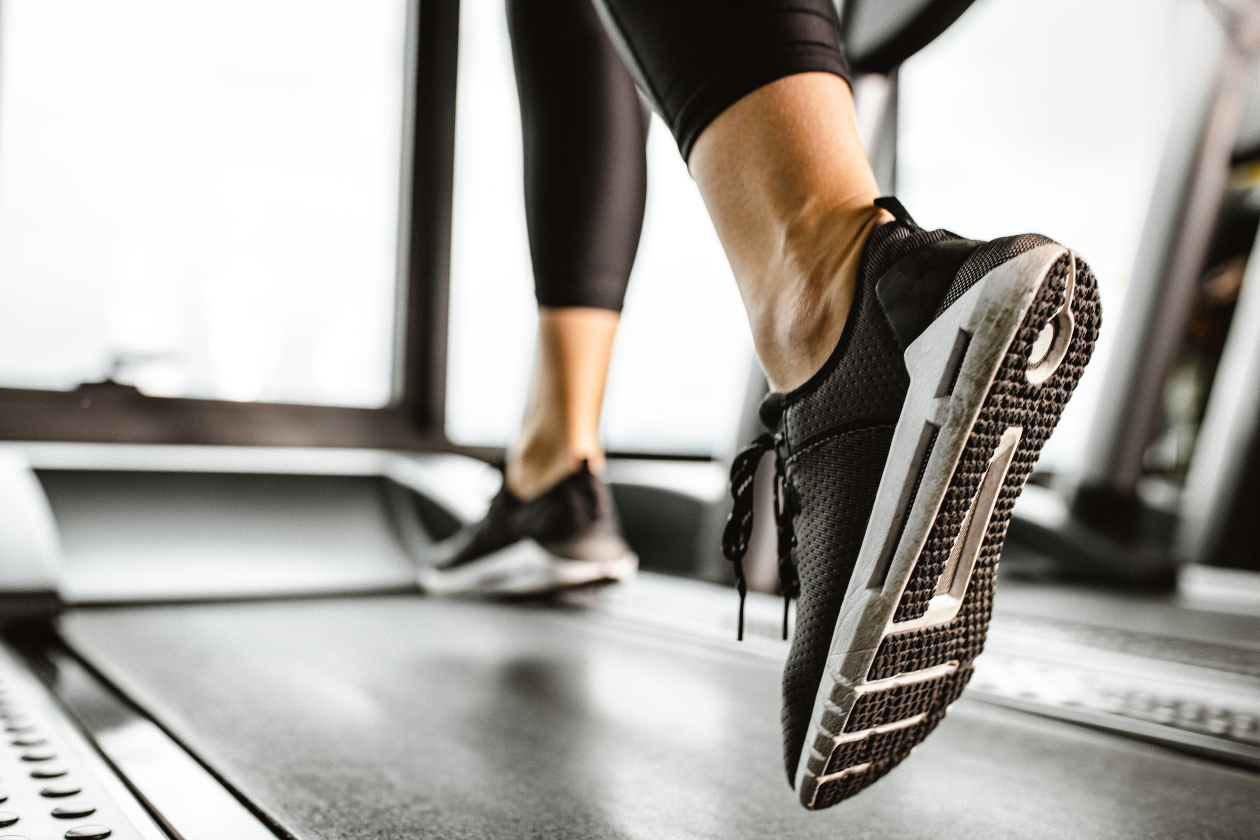 Close up of unrecognizable athlete running on a treadmill in a gym.