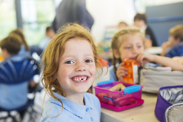 Smiling Girl Missing a Tooth With a Healthy Lunch